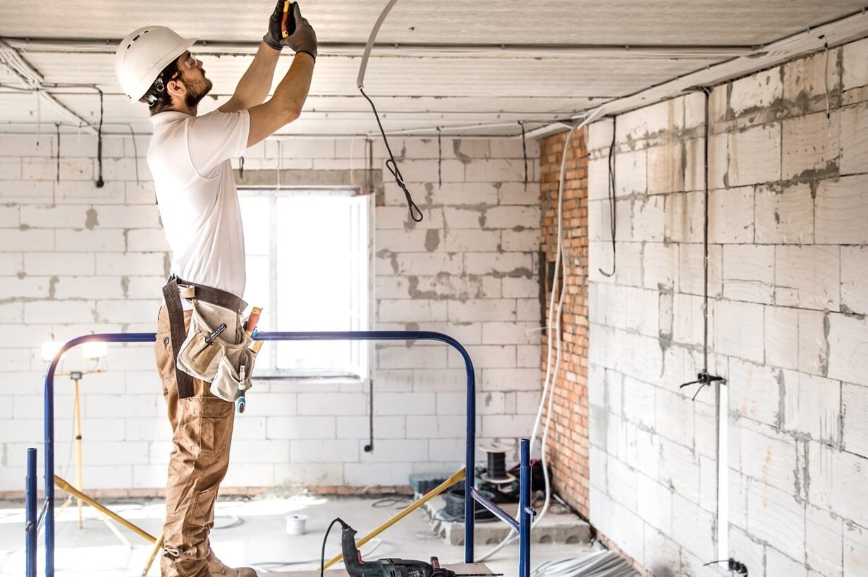 Electrician installer with a tool in his hands, working with cable on the construction site.